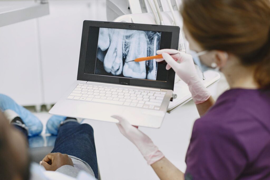 Dentist explaining dental x-ray results to a patient using a laptop in a clinic.